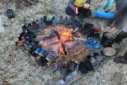 chaussures-et-chaussettes-mouillees-disposees-en-cercle-autour-d-un-feu-de-camp-pour-secher-tandis-que-des-campeurs-preparent-de-la-nourriture-dans-une-marmite-sur-le-feu